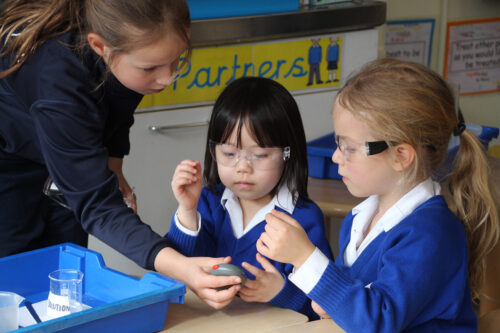 Year 6 and Year 1 girls looking at a stop watch as part of a science experiment.