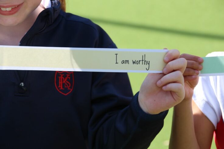 Girl holding piece of paper that says 'I am worthy'.