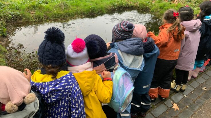 Ken Prep girls in colourful coats looking at pond.